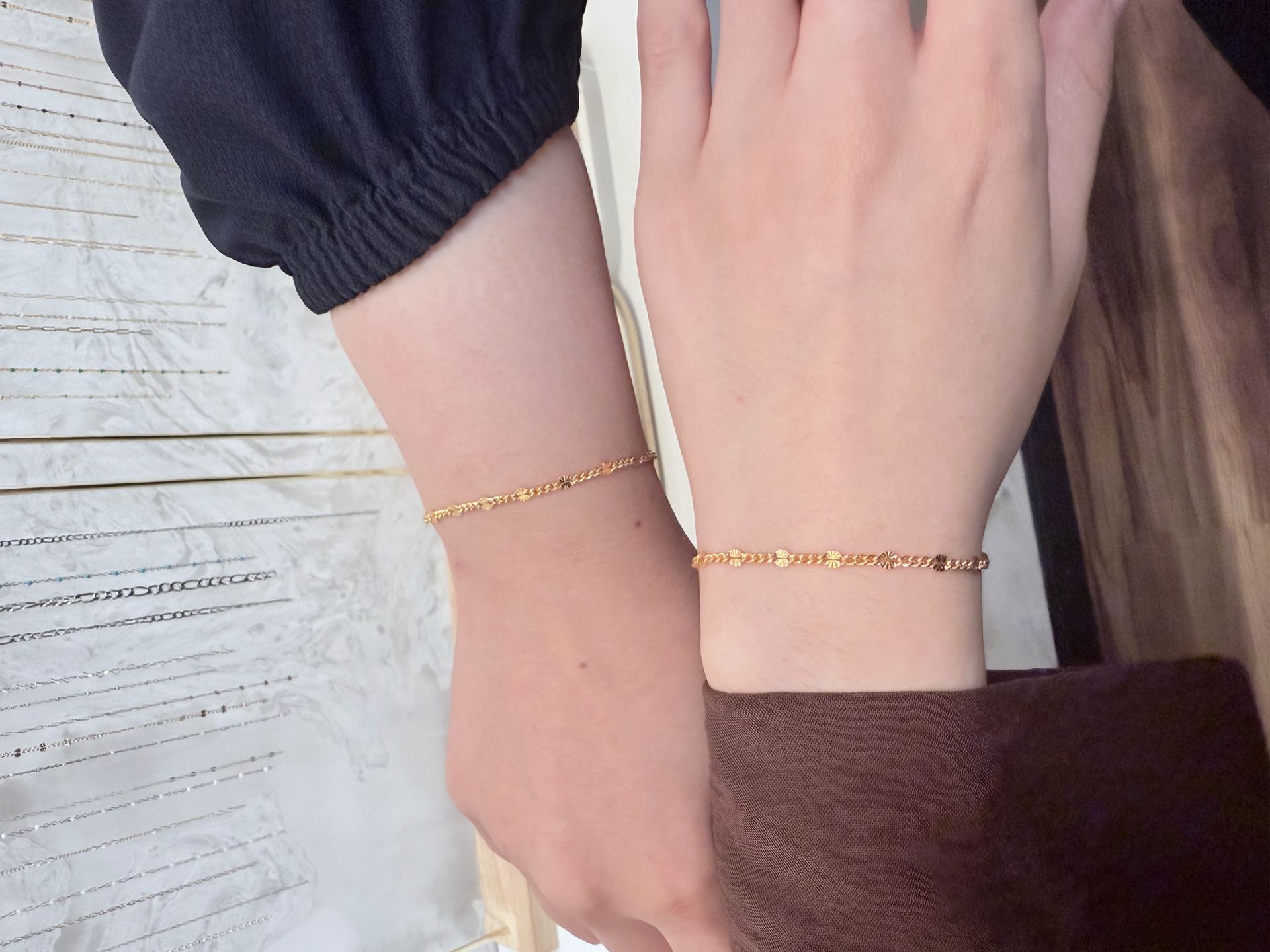 Two wrists wearing matching textured gold bar-link bracelets, one rose gold and one yellow gold